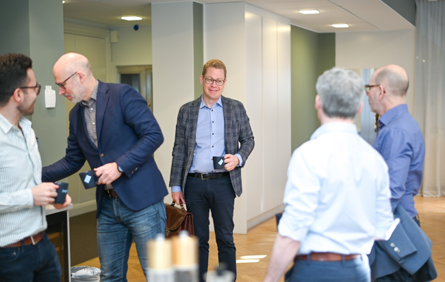 En grupp män som står med kaffekopar i handen och samtalar.
