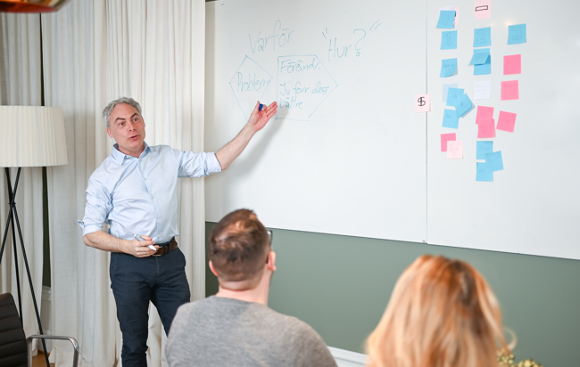 En man som står framför en en whiteboard med en grupp människor.