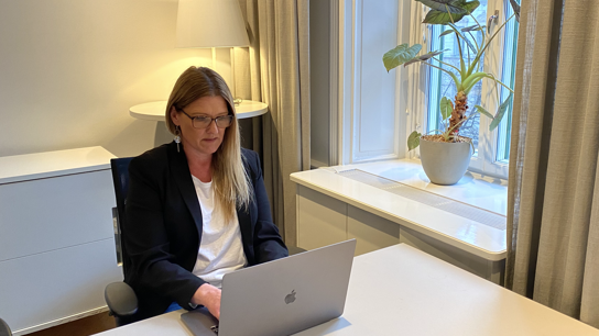 En kvinna sitter vid ett bord och skriver på en Mac-dator, omgiven av en modern och fokuserad arbetsmiljö.
