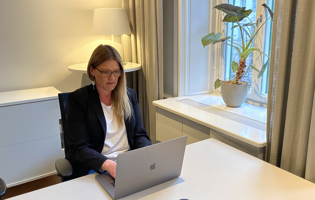En kvinna sitter vid ett bord och skriver på en Mac-dator, omgiven av en modern och fokuserad arbetsmiljö.