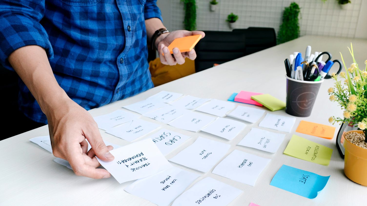 En person som organiserar post-it lappar med skriven text på ett bord.