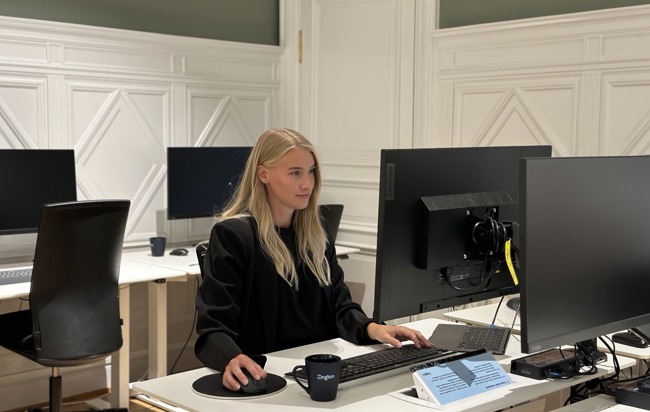 En kvinna som sitter vid en bord med en dator
