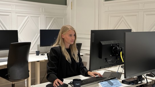 En kvinna som sitter vid en bord med en dator