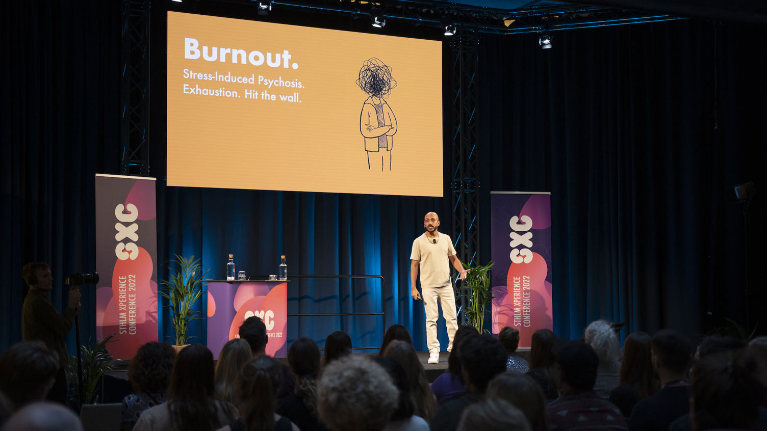 Talare på eventet SXC. Ordet burnout visas på en skärm. Året är 2022.