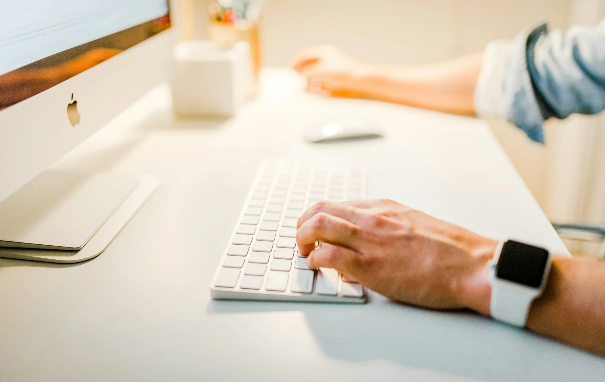 En person som skriver på sin vita keyboard och mus med sin Apple skärm