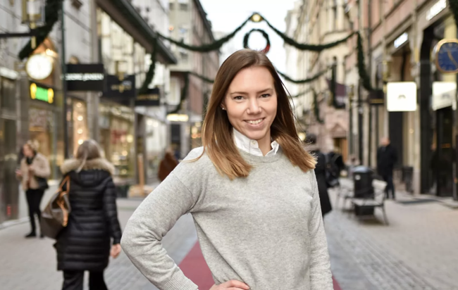 En kvinna i vit tröja poserar för en bild på en gågata.
