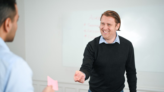 En man som räcker över en post-it lapp till en annan man.