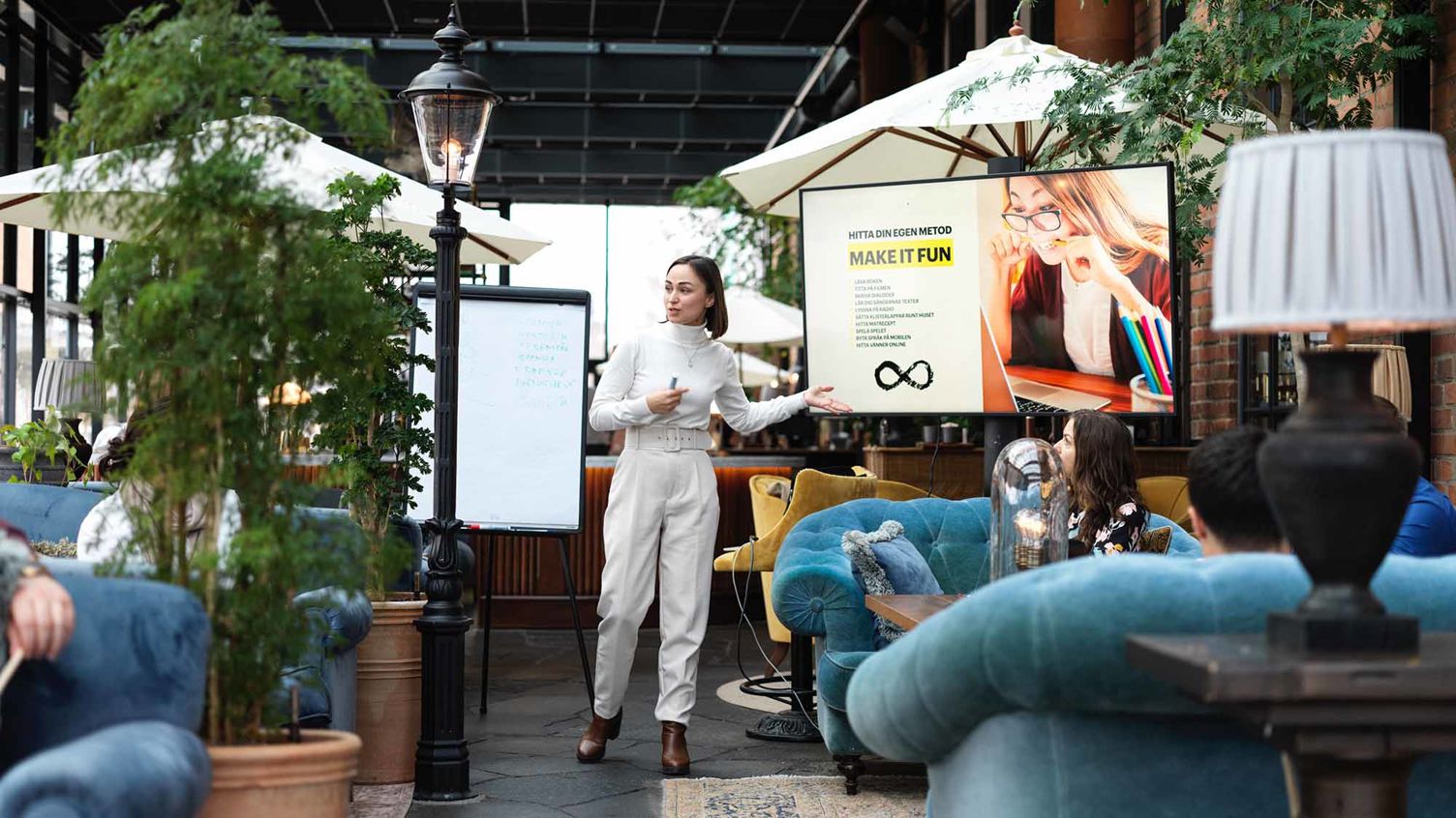 En kvinna håller en presentation framför en skärm på en innergård.