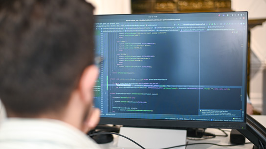 En man som sitter framför en datorskärm och tittar på kod och tycks programmera.