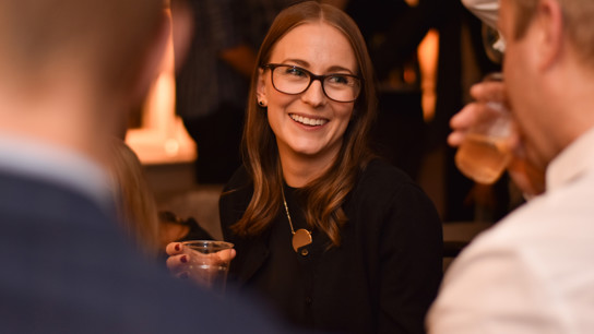En kvinna med ett vattenglas i handen ler mot en man som dricker ur sitt glas, i en avslappnad och social atmosfär.