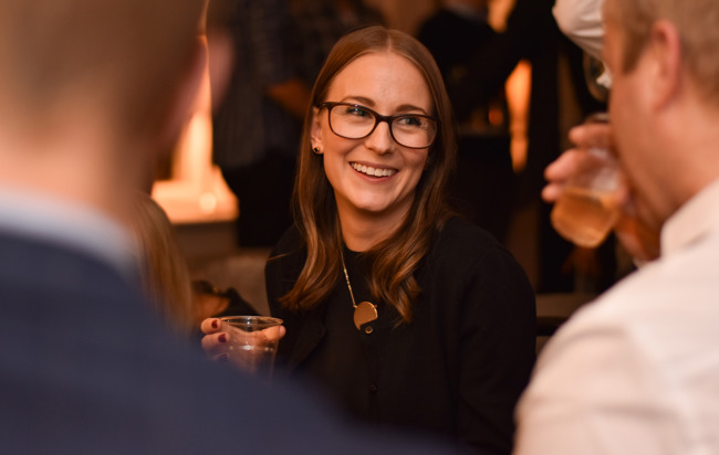 En kvinna med ett vattenglas i handen ler mot en man som dricker ur sitt glas, i en avslappnad och social atmosfär.