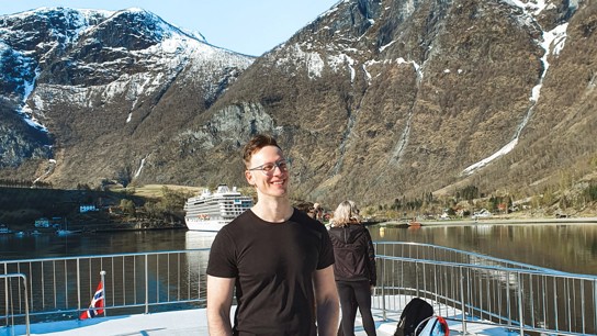 Porträttbild Lucas Lucchi i en fjord med en scenisk bakgrund av berg.