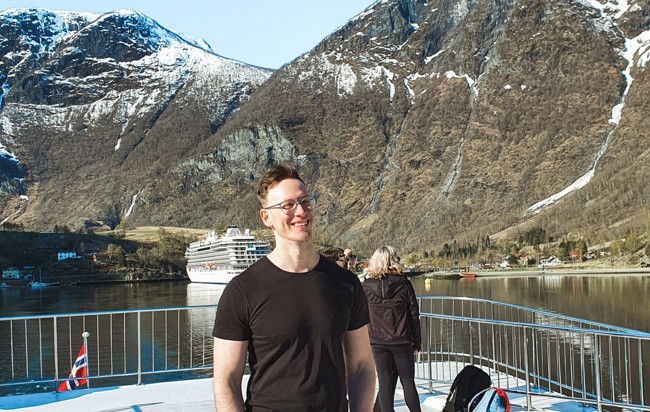 Porträttbild Lucas Lucchi i en fjord med en scenisk bakgrund av berg.