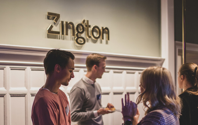 En grupp människor som som står och pratar vid receptionsdisken på Zington.