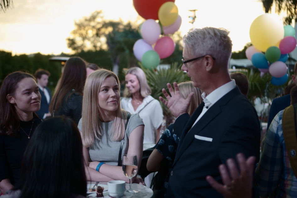 En utomhus fest och en man som pratar med en kvinna med ballonger i bakgrunden.
