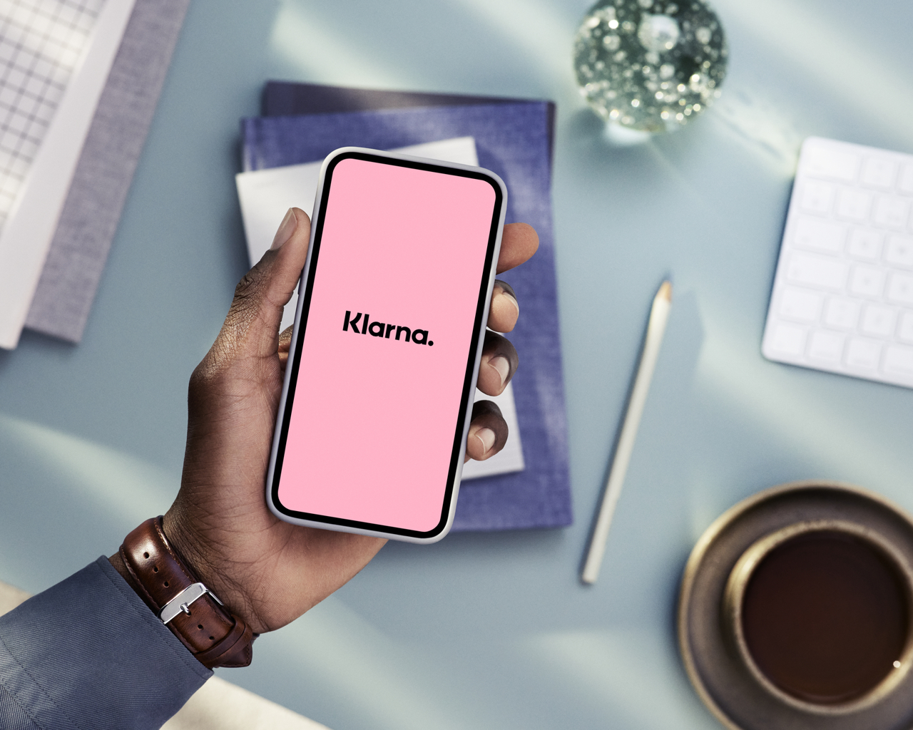 En hand som håller en mobiltelefon och på skärmen står det Klarna.
