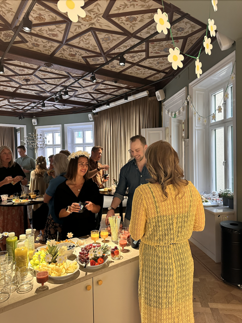 En grupp människor som står runt ett bord med frukt och drinkar.
