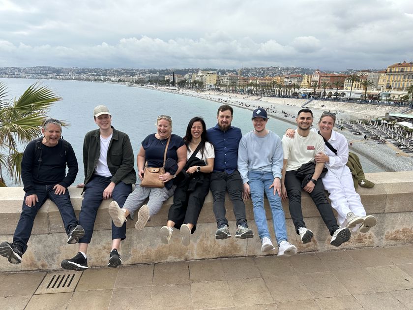 En grupp människor som sitter på en mur med solstrand och hus i bakgrunden.