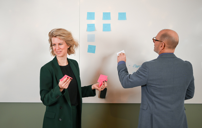 Två personer jobbar med post-it lappar vid en whiteboard tavla.