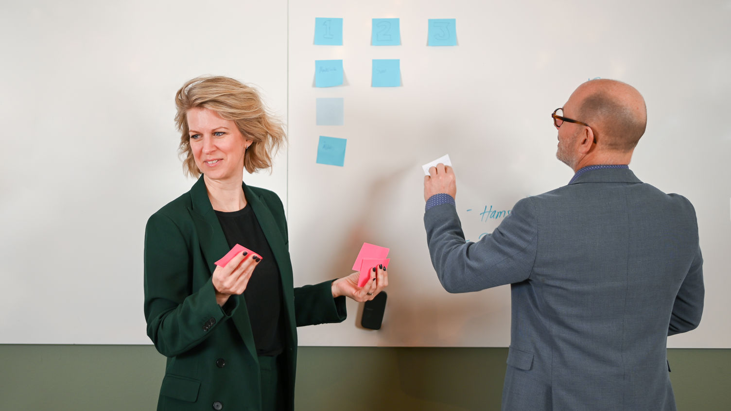 Två personer jobbar med post-it lappar vid en whiteboard tavla.