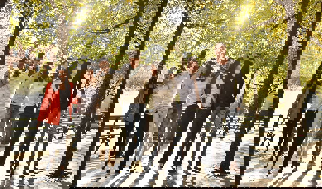 En grupp glada människor poserar för en bild i en park med solen bakom sig.